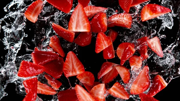 水のスプラッシュでスライスされたイチゴの凍結運動 黒の背景に隔離 — ストック写真