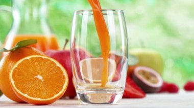 Multivitamin suyunu cama dökmenin süper yavaş bir yolu. Soyut yeşil arkaplanı olan beyaz masaya yerleştirilmiş. Yüksek hızlı sinema kamerası, 1000 fps..