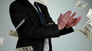 Gri arka planda izole edilmiş uçan dolarlarla el çırpan genç bir iş adamının yakın çekimi.