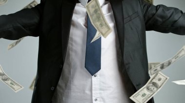 Gri arka planda izole edilmiş dolarlarla uçan genç bir iş adamının yakın çekimi.