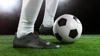 Futbolcu iş başında, topa vurmaya hazır. Arka planda spot ışıkları olan karanlık sahne.