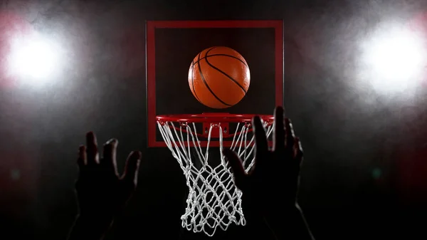 バスケットボール黒の背景にバスケットを通過し 詳細なショット ショットの前に男の手のシルエット — ストック写真