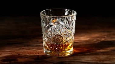 Super slow motion of falling ice cube into whisky drink. Placed on old wooden table. Filmed on high speed cinema camera, 1000fps