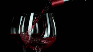 Siyah arka planda izole edilmiş kırmızı şarabın çok yavaş bir şekilde dökülmesi. Hız rampası etkisi. Yüksek hızlı sinema kamerası, 1000 fps.