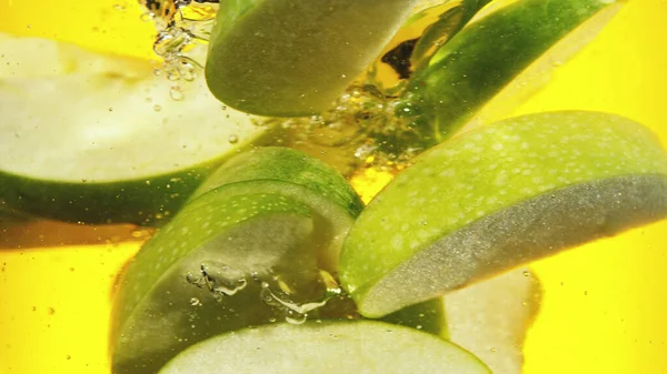 Close Green Apple Slices Water Isolated Yellow Background — Stockfoto