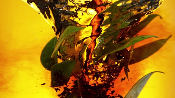 将红茶拌入水中 旋转成螺旋形 里面有新鲜的绿叶 在黄金背景下被隔离 — 图库照片
