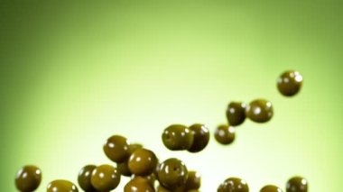 Yeşil arka planda uçan yeşil zeytinlerin süper yavaş çekimi. Yüksek hızlı sinema kamerası, 1000fps.