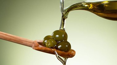 Tahta kaşığa konmuş yeşil zeytinlerin üzerine zeytinyağı dök. Yeşil arkaplanda izole.