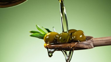 Yapraklı yeşil zeytinlerin üzerine zeytinyağı dök, tahta kaşığa koy. Yeşil arkaplanda izole.