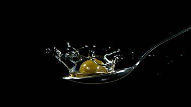 Kaşık üzerine dökülen yeşil zeytin yağı. Siyah arkaplanda izole.