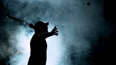 Tenisçi siluetinin topa vuruşunun süper yavaş çekimi. Çevrede duman etkisi, siyah arka plan. Yüksek hızlı sinema kamerası, 1000fps.