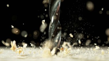 Süper makro çelik matkap ve uçup giden odun parçaları. Talaş, dönen bir matkabın üzerinden uçar. Tahtaya delik açar..