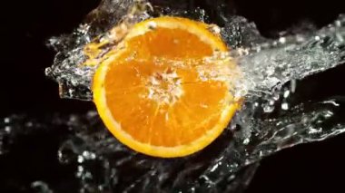 Su Sıçratan Portakal Diliminin Süper Yavaş Hareketi. Dönen Portakal Dilimi ve Sulama Suyu. Kara Arkaplan 'da izole edilmiş. Yüksek Hız Sinema Kamerası, 1000 Fps.