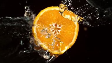 Su Sıçratan Portakal Diliminin Süper Yavaş Hareketi. Dönen Portakal Dilimi ve Sulama Suyu. Kara Arkaplan 'da izole edilmiş. Yüksek Hız Sinema Kamerası, 1000 Fps.