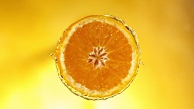 Super Slow Motion of Orange Slice With Water Splashes. Rotating Slice of Orange with Splashing Water Around. Isolated on Colored Background. Filmed on High Speed Cinema Camera, 1000 Fps.