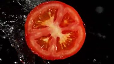 Su Sıçratan Domates Diliminin Süper Yavaş Hareketi. Dönen Domates Dilimi ve Sulama Suyu. Kara Arkaplan 'da izole edilmiş. Yüksek Hız Sinema Kamerası, 1000 Fps.