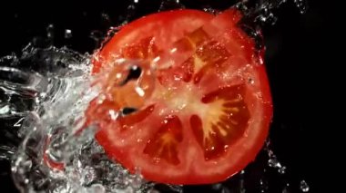 Su Sıçratan Domates Diliminin Süper Yavaş Hareketi. Dönen Domates Dilimi ve Sulama Suyu. Kara Arkaplan 'da izole edilmiş. Yüksek Hız Sinema Kamerası, 1000 Fps.