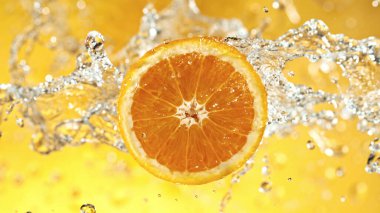 Slice of orange with water splashes on colored background. Isolated studio shot, fresh fruit background.