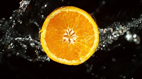 Slice of orange with water splashes on black background. Isolated studio shot, fresh fruit background.
