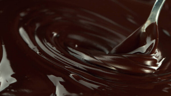 Close-up of stirring stream of melted chocolate, creating smooth shapes.