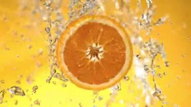 Super Slow Motion of Orange Slice With Water Splashes. Rotating Slice of Orange with Splashing Water Around. Isolated on Colored Background. Filmed on High Speed Cinema Camera, 1000 Fps. Speed Ramp.