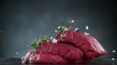Flying pieces of raw beef steaks falling on table with spice. Filmed on high speed cinema camera, 1000 fps. Speed ramp effect.