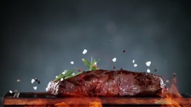 Flying pieces of grilled beef steak and spices falling on table with fire. Filmed on high speed cinema camera, 1000 fps. Speed ramp effect.
