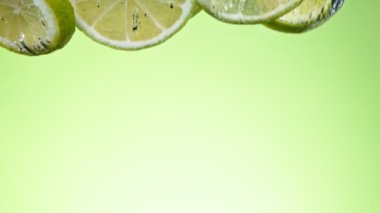 Super slow motion of falling lime slices into water, green background. Filmed on high speed cinema camera, 1000 fps.
