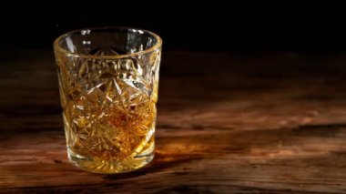Super slow motion of falling ice cube into whisky drink. Placed on old wooden table. Filmed on high speed cinema camera, 1000fps