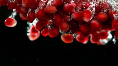 Nar parçalarının suya düşmesi çok yavaş bir hareket. Siyah arka planda izole edilmiş. Yüksek hızlı sinema kamerası, 1000fps