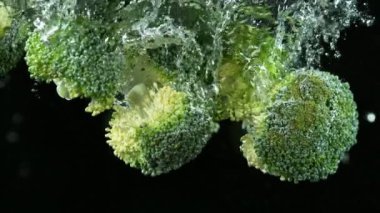 Brokoli parçalarının suya düşmesi çok yavaş bir hareket. Siyah arka planda izole edilmiş. Yüksek hızlı sinema kamerasıyla çekildi, 1000fps. Hız rampası etkisi.