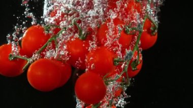 Kirazlı domateslerin suya düşmesi çok yavaş bir hareket. Siyah arka planda izole edilmiş. Yüksek hızlı sinema kamerasıyla çekildi, 1000fps. Hız rampası etkisi.