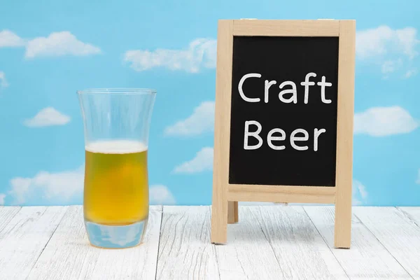 天気の良い空と木の上に黒板とビールの冷たいガラスとクラフトビールの看板 — ストック写真