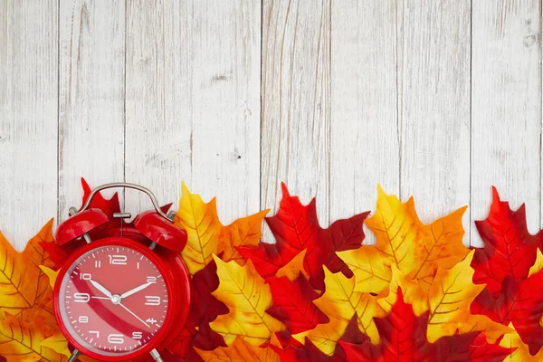 赤と黄色の秋の葉を持つ赤い目覚まし時計はあなたの季節のメッセージのための風化した木で背景に落ちる — ストック写真