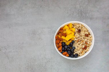 Yulaf ezmeli yulaf lapası, yaban mersini, mango ve yukarıdan beton gri masada badem. Düz çizgi. Sağlıklı kahvaltı. Boşluğu kopyala