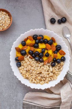 Yulaf ezmeli yulaf lapası, yaban mersini, mango ve yukarıdan beton gri masada badem. Düz çizgi. Sağlıklı kahvaltı. Boşluğu kopyala