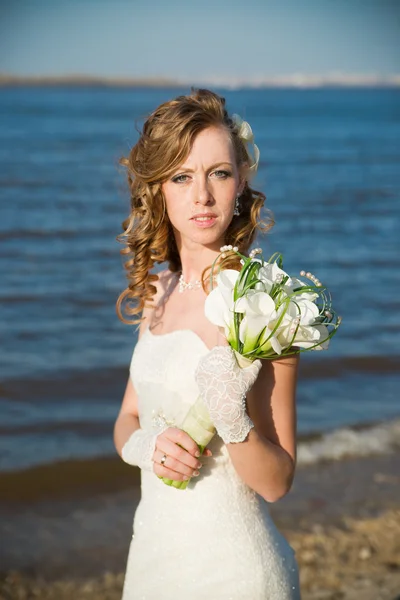 Hermosa novia con un ramo de lirios de cala en la costa del río —  Fotos de Stock