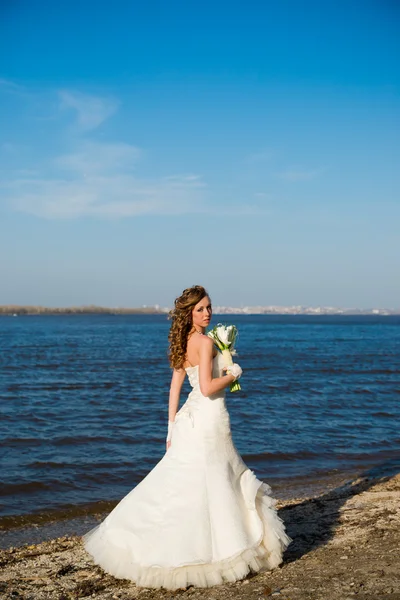 Beautiful bride in a white dress on coast of river — Stock Photo, Image