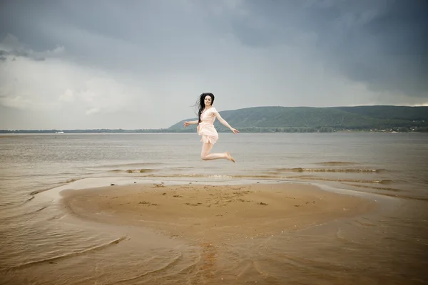 Beautiful young woman jumping on a sandy beach — Stock Photo, Image