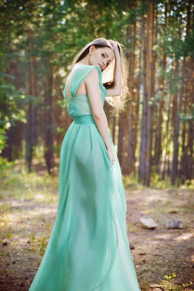 Mooie jonge vrouw in een turquoise jurk in een dennenbos — Stockfoto