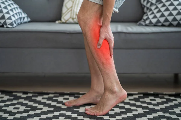 The man\'s calf muscle cramped, massage of male leg at home, painful area highlighted in red