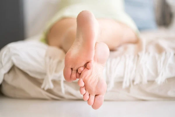 Woman relaxing in bedroom, female feet close-up, foot care concept, home interior