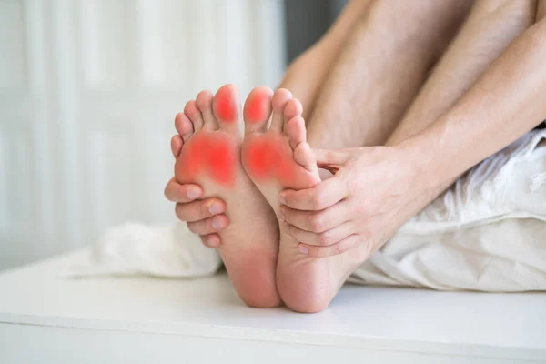 Foot pain, man suffering from feet ache in home interior, podiatry concept