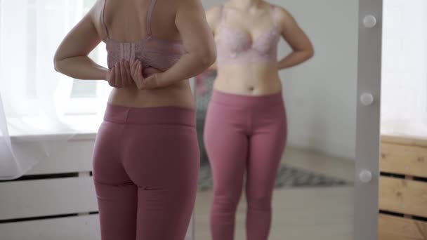 女性はフィッティングルームでブラにしようとします ワイドクラスプを持つ巨乳は ミラーに反映されています クローズアップ4Kビデオ — ストック動画