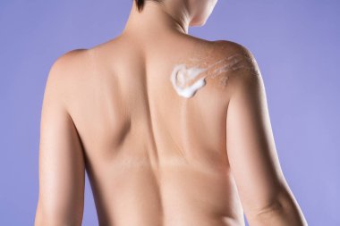 Kadın omzuna köpük sürüyor mor arka planda, vücut bakımı konsepti