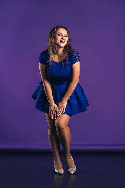Счастливая модель plus size в синем платье на фиолетовом фоне, положительная концепция тела