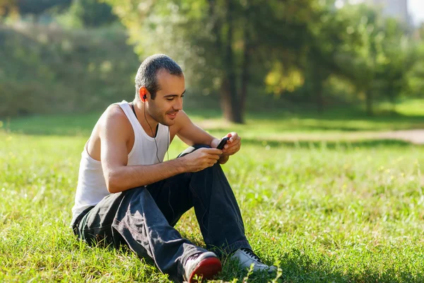 Guy listening to the player sitting on the grass — Stockfoto