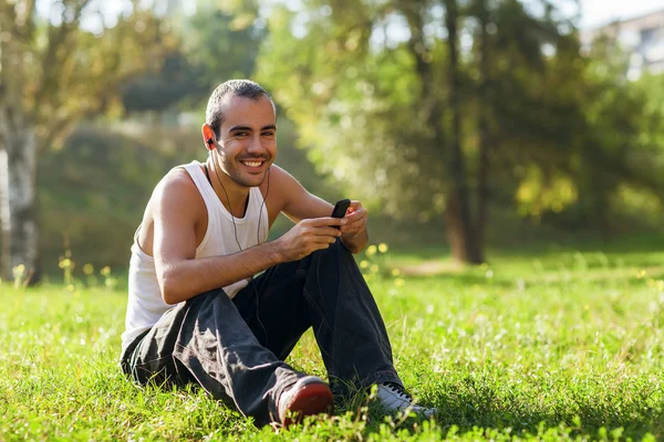 Oyuncu ve gülüyor dinlerken çimlerin üzerine oturan adam — Stok fotoğraf