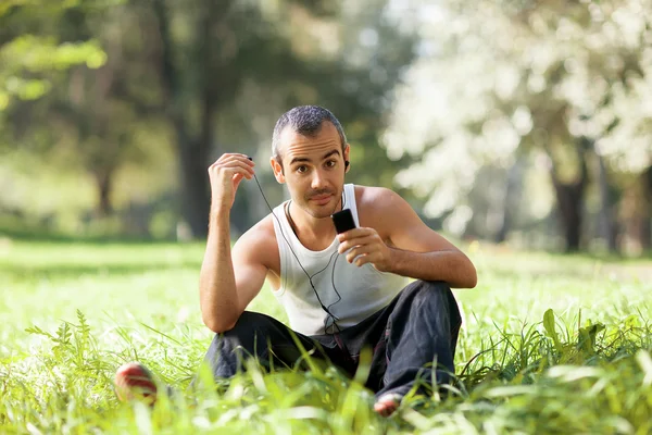 Le gars assis sur l'herbe écoute le joueur et regarde — Photo