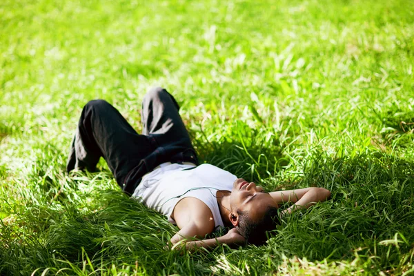 Gelukkig man liggen op het gras en luisteren naar muziek — Stockfoto